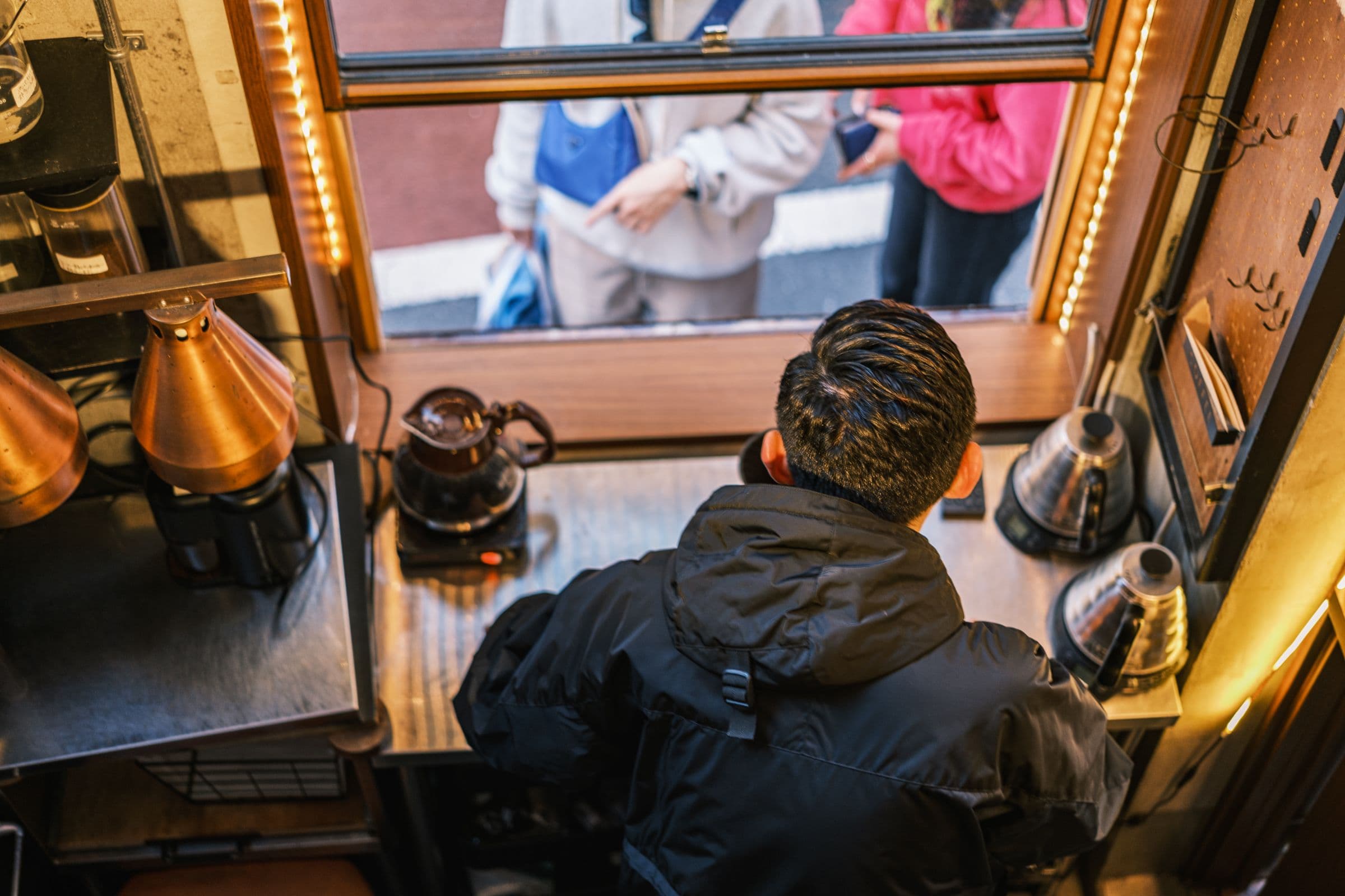 COFFEE SHOPの窓越しにコーヒーを提供するスタッフ