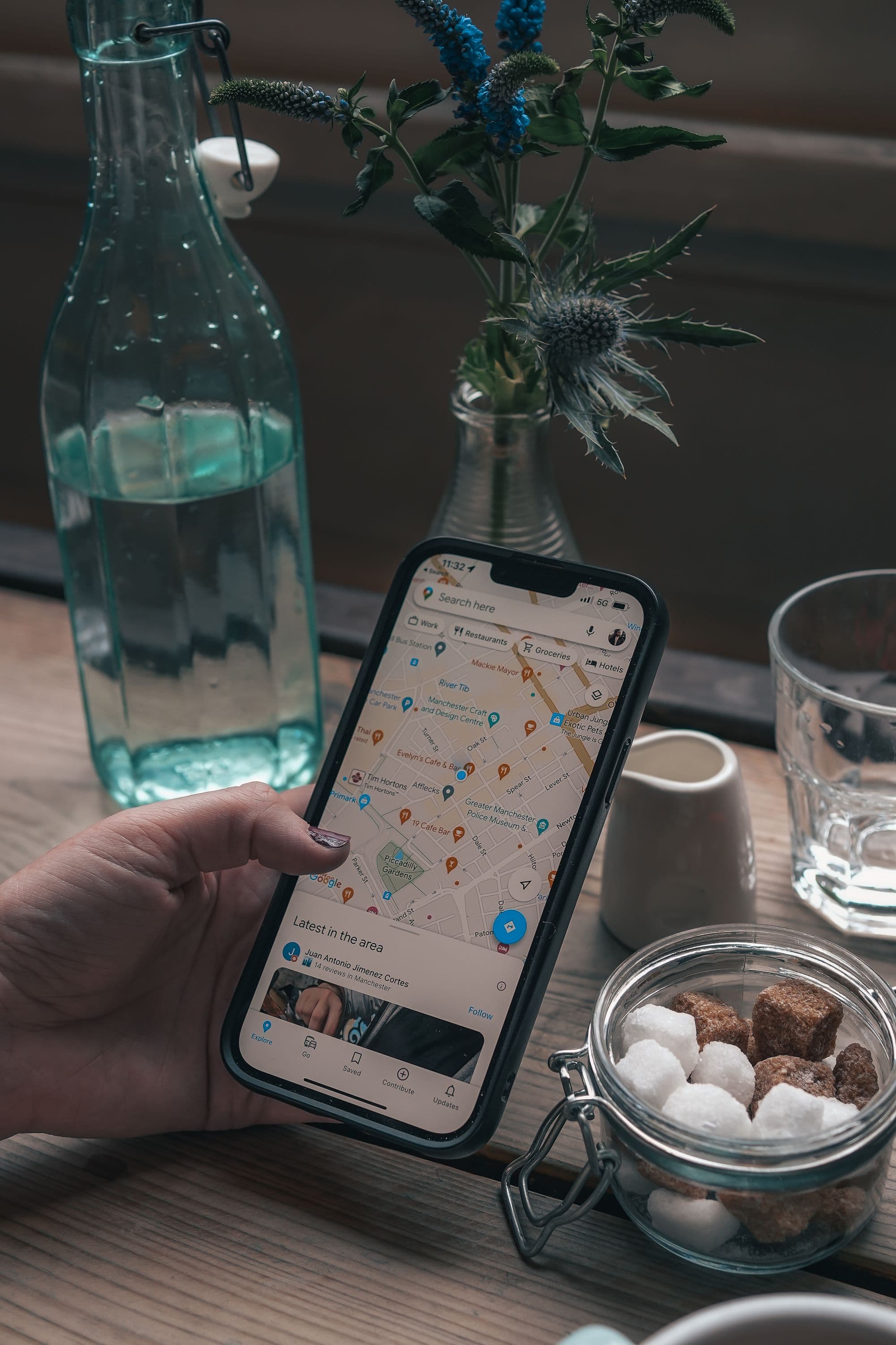 カフェのテーブルで、周辺の店舗が並ぶ地図アプリの画面をスマートフォンで見ている様子